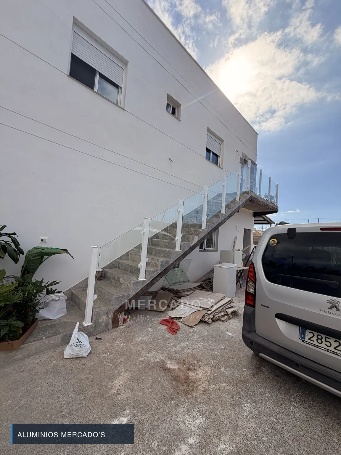 Barandilla de escalera con vidrio transparente y postes blancos durante la obra